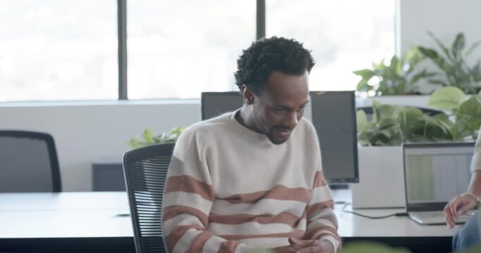 Coworkers at office, man checking phone opening notebook writing while woman leaning on desk