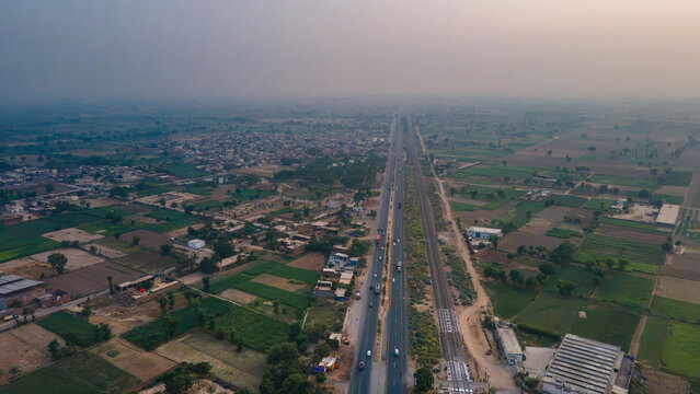 Aerial view of a Multan road highway and parallel railway line cutting through agricultural fields and small settlements in the rural landscape of Punjab, Pakistan.