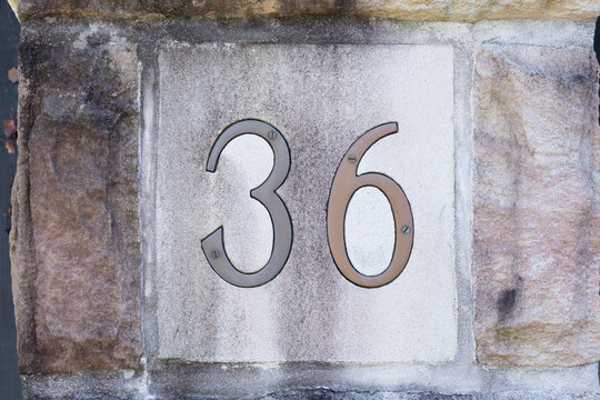 Number thitysix made with brass for address label on house. Number on smooth sandstone background