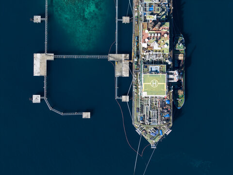 Aerial view of a Floating Storage and Offloading Ship with a helipad moored to a pier in clear blue water in Buleleng Regency, Bali, Indonesia.