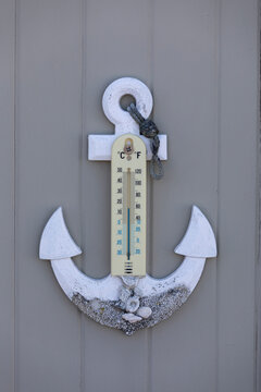 Anchor and thermometer gate decoration with sea shells forming a nautical theme in light blue and gray wood.