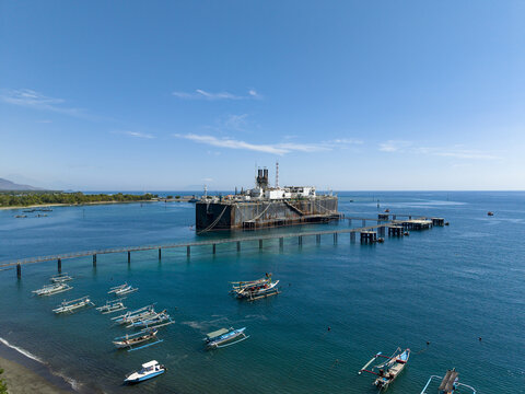 Aerial view of a Floating Storage and Offloading Ship anchored in the sea with a long pier and traditional fishing boats in Buleleng Regency, Bali, Indonesia.
