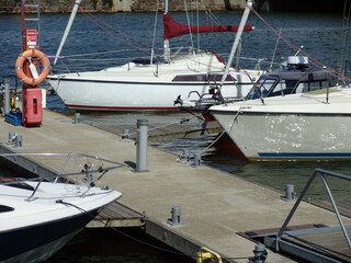 Sailboats moored at floating docks in a modern marina, featuring white hulls, rigging, life‑saving equipment, and calm harbor waters in a recreational boating setting. © Martins