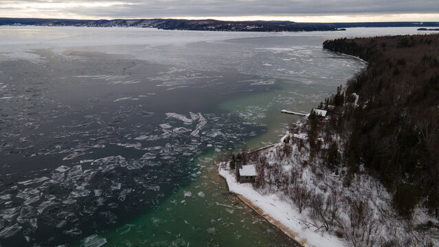 Aerial view of Grand Island Lighthouse situated on a snow-covered shoreline with ice floes drifting in the cold waters of Lake Superior in Munising, Michigan, United States.