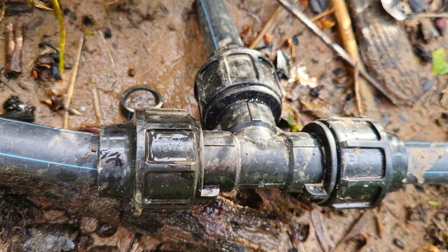 HDPE pipe compression fitting T joint connected to blue PVC water pipe outdoors. Close up of HDPE pipe joint connector connected to PVC pipe passing through wall