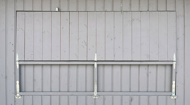 Close‑up of a gray wooden gate with vertical planks, metal hinges, and structural bracing, creating a minimalist architectural background with clean lines and subtle texture.