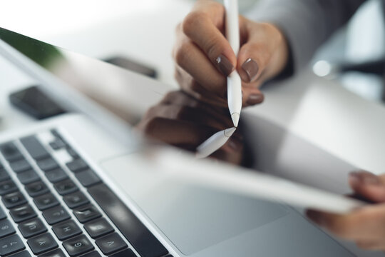 Business woman using stylus pen on digital tablet, proofreading e-document before signing with laptop on office desk, corporate business, close up