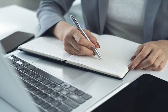 Business woman hand writing on notebook at office with laptop computer on office desk, online research with laptop. remote work and meeting agenda, business planning
