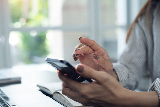 Close-up of woman using smartphone while working on laptop, searching online content at home office, online business