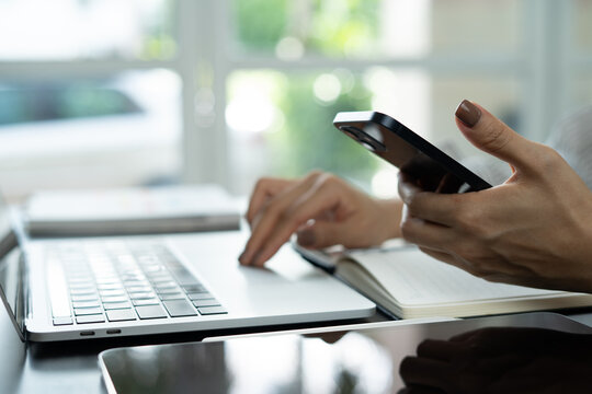 Close-up of business woman using smartphone while working on laptop computer, searching online content at home office, online business, Student studying online. Business background