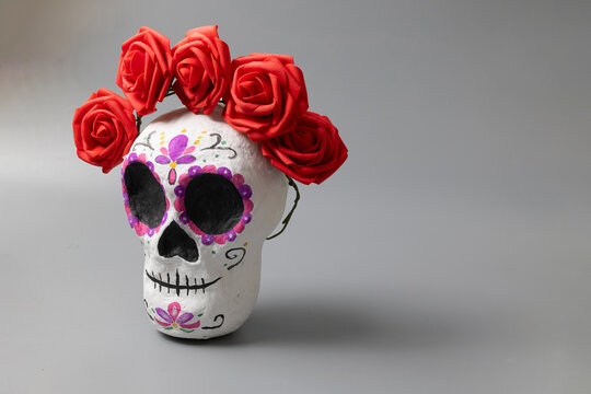 Handmade Day of the Dead sugar skull crafted as a decorative folk-art piece; painted facial motifs, a red fabric rose crown, and a festive color palette, shown in a simple studio for DIY decor.
