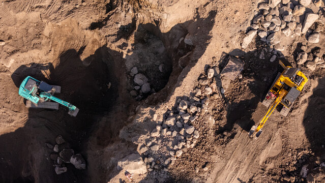 Aerial view of two excavators working in a large quarry with piles of rocks and dirt in Klaten, Central Java, Indonesia.