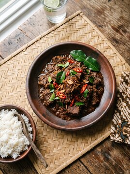 Traditional Indonesian beef rendang served with white rice on a rustic wooden table.