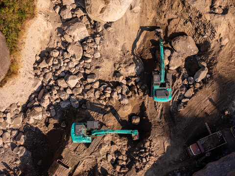 Aerial view of two excavators working in a stone quarry with large boulders and a truck in Klaten, Central Java, Indonesia.