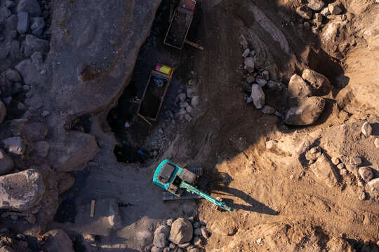 Aerial view of an excavator working in a rocky quarry with trucks parked nearby in Klaten, Central Java, Indonesia.