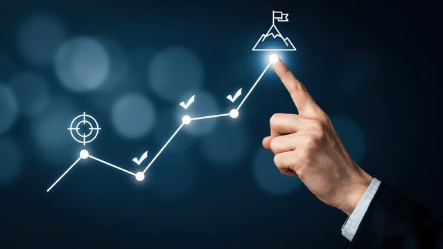 Business hand pointing at a glowing mountain peak target on an upward growth graph, symbolizing goal achievement and success.