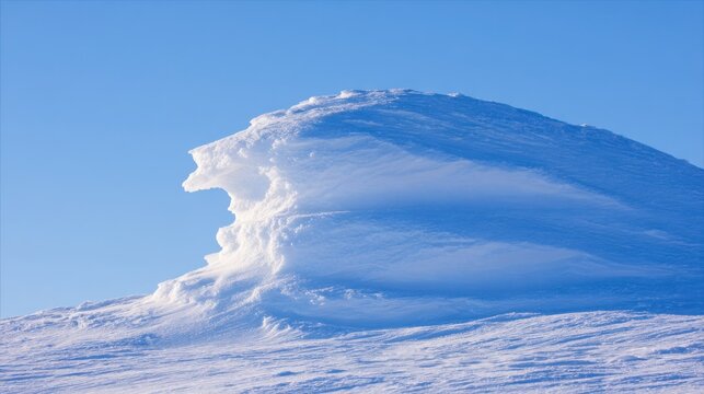 Majestic snow cornice formation sculpted by wind on a windswept ridge against a clear blue sky