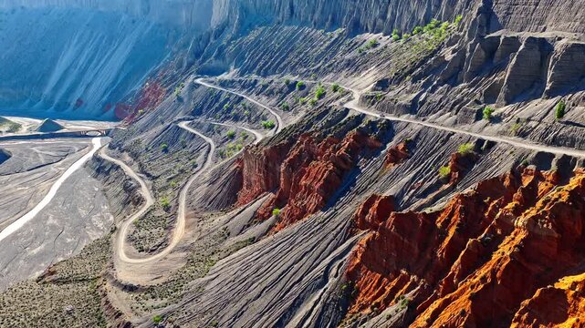 Aerial view of a winding road curving through a steep and colorful mountain canyon in Anjihai Grand Canyon, Xinjiang, China.