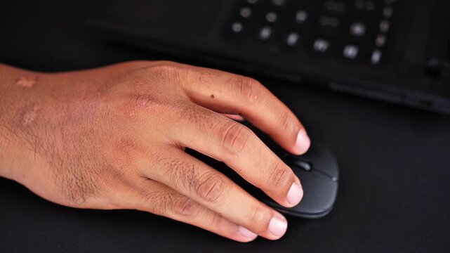 Close-up of a Person's Hand Using a Black Computer Mouse on a Dark Office Desk