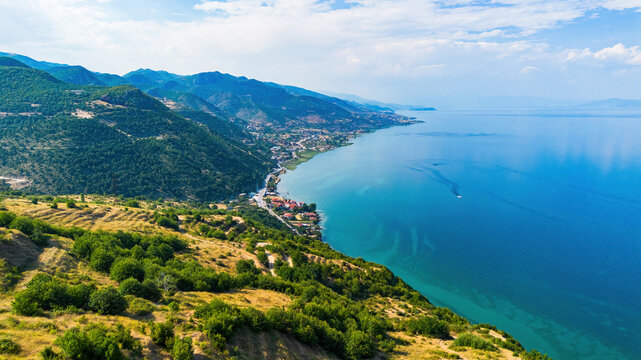 Aerial drone view of the mountainous coastline, coastal villages, and a boat cruising on Lake Ohrid near Pogradec, Albania
