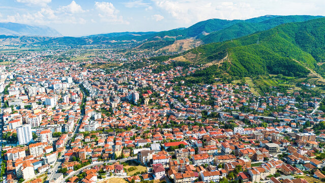 Aerial drone view of the dense urban neighborhoods, residential buildings, and green hills of Pogradec, Albania