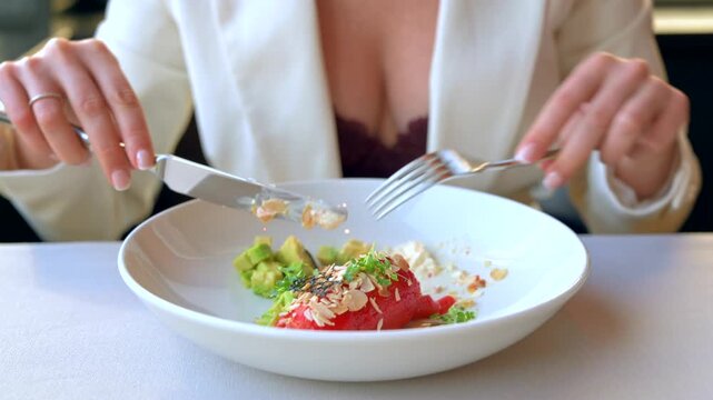 Woman dining on avocado and salmon tartar with almonds and microgreens, close up shot.