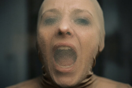 Surreal portrait of a screaming face tightly covered and distorted by a stretchable beige fabric