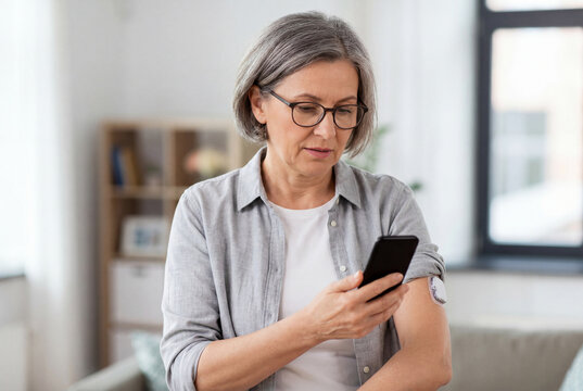 Older woman with grey hair looking at her smartphone while wearing a glucose monitor on her arm