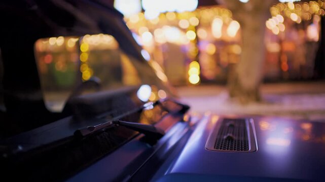 Evening city street view from car hood with festive lights reflection and bokeh creating a magical atmosphere.