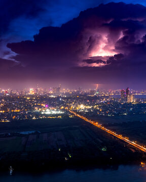 Aerial view of the illuminated Hanoi skyline at night under a dramatic thunderstorm with lightning striking through dark clouds above the urban landscape and a bridge Hanoi, Ha Noi, Vietnam.
