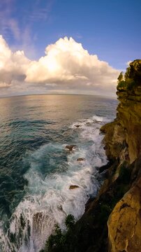 Vertical slow motion panning video of Sydney's rocky coastline and ocean with towering clouds in the distance, captured with a fisheye lens.