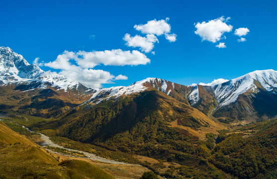 Landscape photograph of snow covered mountains and glacier river valley viewed from Chkhutnieri pass in Svaneti Georgia.