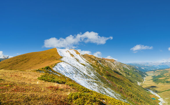 Landscape photograph of snowy ridge line and golden hill at Chkhutnieri pass overlooking Adishi valley in Svaneti Georgia.