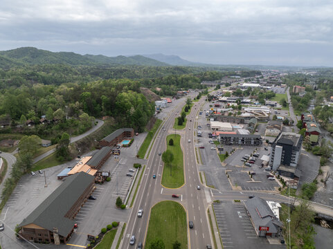 Aerial view of the town of Pigeon Forge featuring a multi-lane road, surrounding hotels, commercial buildings, and lush green hills in Pigeon Forge, Tennessee, United States.