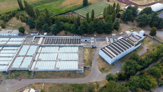 Aerial view of the Assago Water Treatment Plant featuring large rectangular filtration tanks with translucent covers, industrial buildings, and surrounding green space in Assago, Lombardy, Italy.