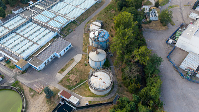 Aerial view of the wastewater treatment facility with anaerobic digesters for sludge processing and biogas production, surrounded by industrial infrastructure in Assago, Lombardy, Italy.