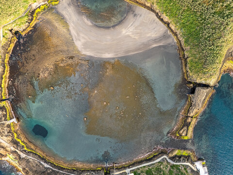 Aerial view of the volcanic crater islet Ilheu de Vila Franca do Campo with its circular lagoon, sandy beach, and rocky cliffs surrounded by the Atlantic Ocean in Sao Pedro, Acores, Portugal.