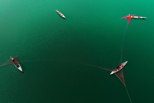 Aerial view of traditional wooden fishing boats casting nets into the calm green river waters in Bogura, Rajshahi Division, Bangladesh.