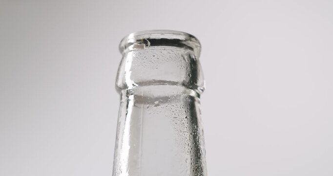 Slow-motion close-up of opening the cap of a chilled glass bottle with a metal bottle opener, showing the cap flying off against an isolated white background, perfect for beverage advertising