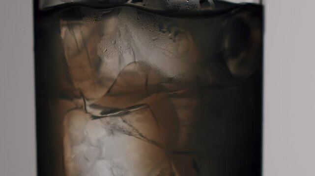 Close-up of ice cubes swirling and melting inside a glass of refreshing cold brew coffee or cola, Ice cubes swirling in a refreshing cold brew coffee drink.