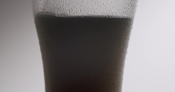 Slow motion shot showing a bartender pouring a cold, dark stout beer with thick foam into a tall, chilled glass covered with condensation droplets, all isolated on a white background