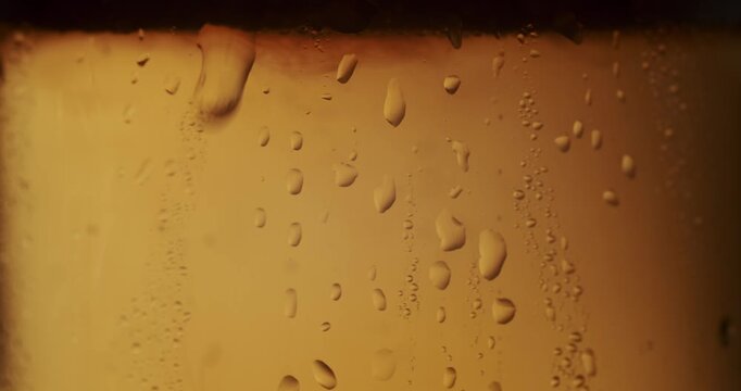 Extreme close-up of a single water droplet sliding down the side of a cold, freshly poured glass of golden beer, slow motion. Condensation droplet sliding down a cold beer glass