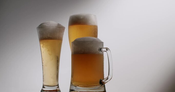 Three rotating glasses of fresh, cold lager and wheat beer with a lot of foam isolated on a white background. Delicious frosty beverage for a pub party or celebration in slow motion