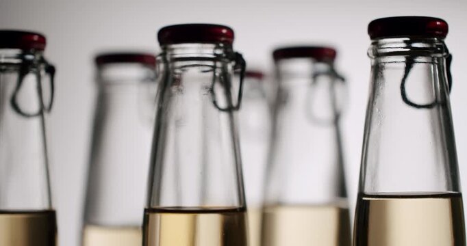 Slow motion footage showing the liquid level in a row of glass bottles with swing top caps mysteriously decreasing, A close-up shot highlighting the colors and reflections of the alcoholic beverages.