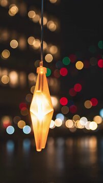video of a glowing orange star ornament hanging outdoors at night. The star gently sways in a subtle night breeze while its inner light softly glows. In the background