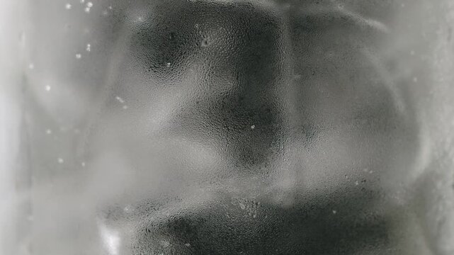 Clear fizzy drink with ice cubes inside a glass, showing bubbles rising slowly to the surface. Refreshing sparkling mineral water or tonic perfect for a cool beverage on a hot summer day.