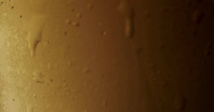 Golden light beer chilling in a glass with condensation drops sliding down in slow motion, Refreshing pint of cold light beer slowly rotating in a glass covered with condensation drops, golden color