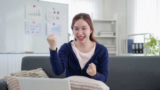 Young Asian professional celebrating success during video call in bright modern home office with copy space