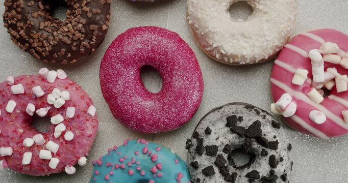 Mouthwatering assortment of delicious sweet doughnuts with multicolored glaze and various toppings rotating on a plate, creating a tempting and colorful display of popular junk food