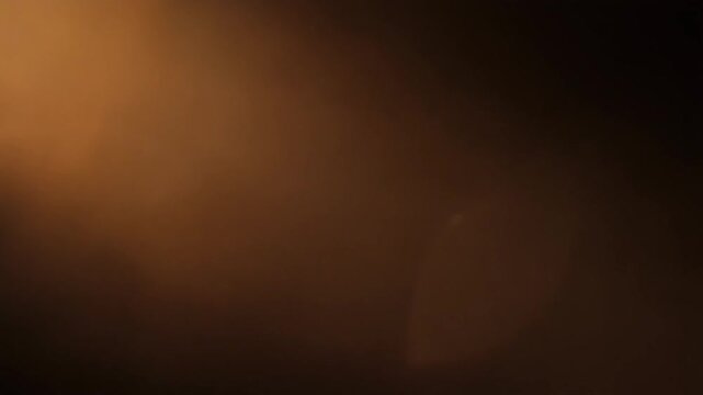 Warm amber light leak bleeds and spreads diagonally across a dark frame with soft organic edges, self-illuminated against total black &mdash; loop ideal for cinematic, retro, and film overlays.